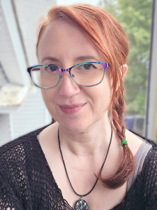 Portrait of a white woman with red hair and a black mesh sweater.